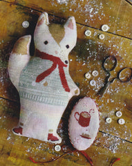 A cross stitch pillow of a woodland fox with a winter scarf, and cup of hot cocoa needlebook next to it.
