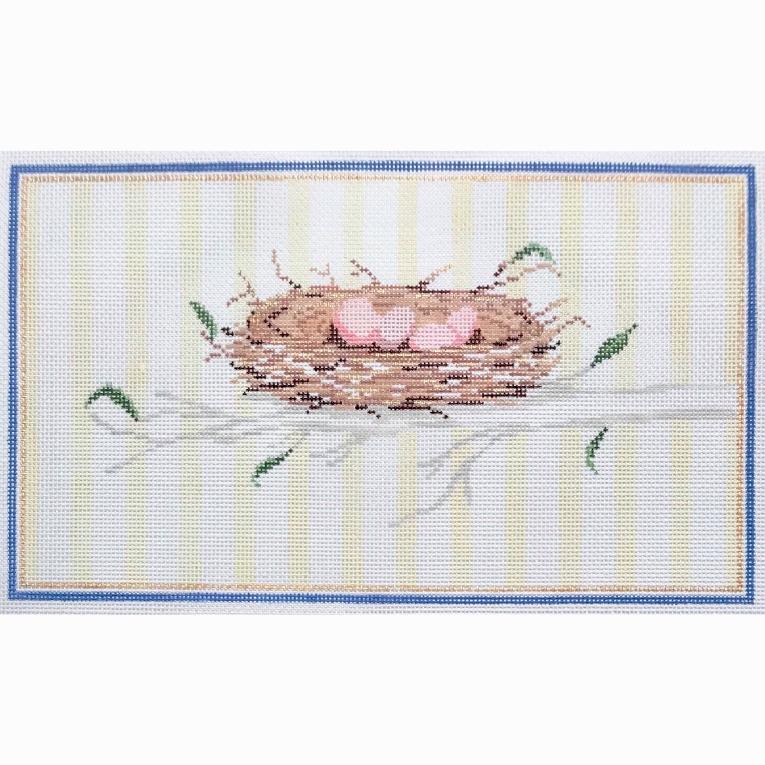 Needlepoint canvas featuring a bird’s nest with three pale pink eggs resting on a branch, surrounded by delicate green leaves and framed by a blue and gold border on a soft striped background.