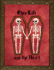 Cross stitch showing two skeletons lying in side‑by‑side coffins and holding hands, with the text “This Life” above and “and the Next” below, stitched on a red background and framed in a rustic metal‑style frame.