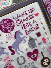 Close up view of same cross stitch with a zoom in on the text, “Wake up snakes, bite a biscuit.”