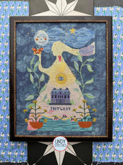Framed cross‑stitch of a tall figure with flowing hair holding a butterfly with a smiling moon and stars above, a sunburst on the torso, a house below, plants on each side, and the words “Not Lost.”