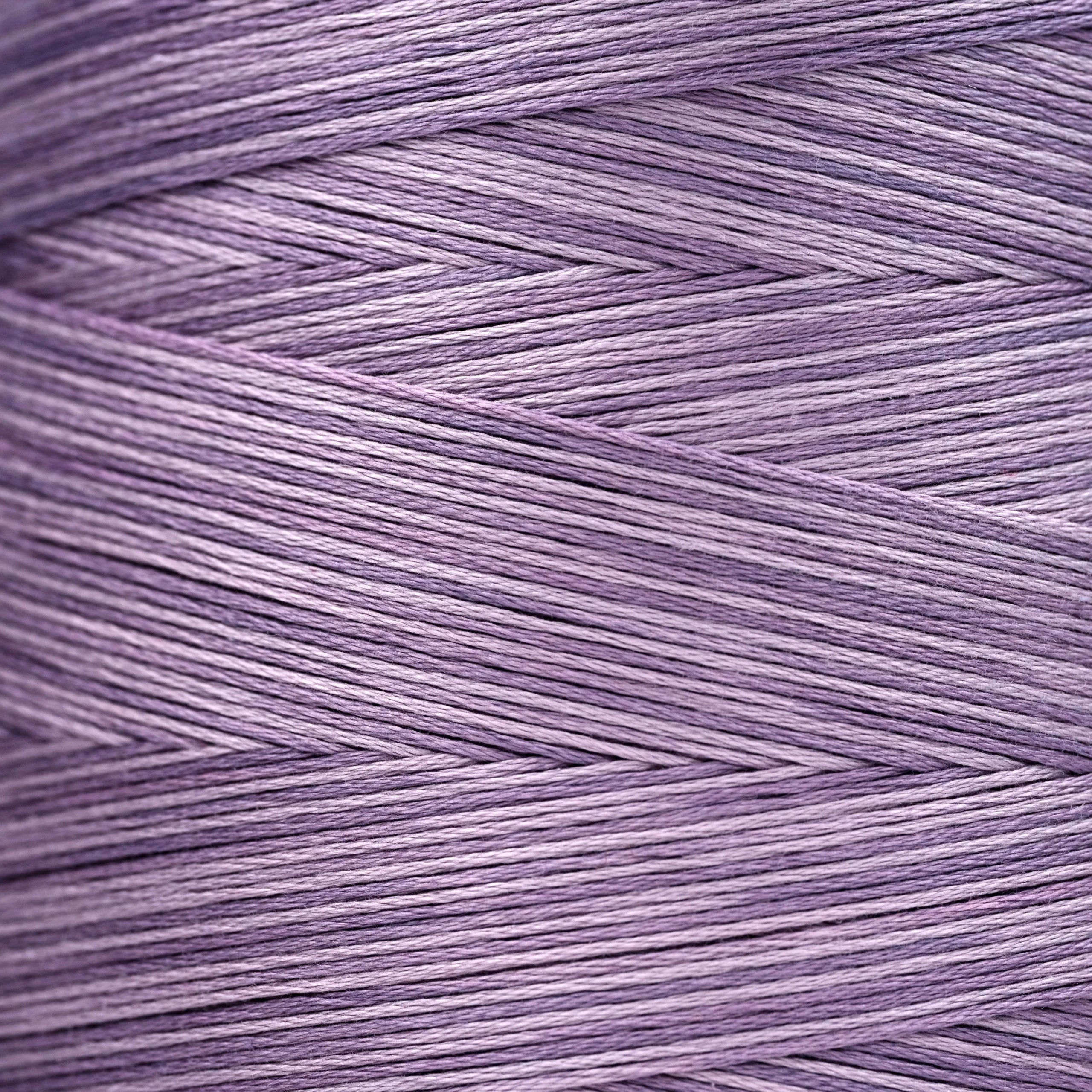 Close-up of lavender‑purple overdyed embroidery floss wound tightly, showing subtle shade variations in the strands.