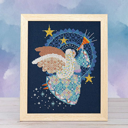 Wood framed cross stitch of an angel in flight, wearing a patchwork skirt, playing a horn, and surrounded by twinkling stars with white wings spread wide.