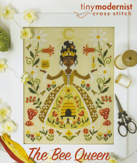 Cross stitch of a Bee Queen in a honey‑gold gown surrounded by buzzing bees, flowers, mushrooms and a tiny beehive scene.