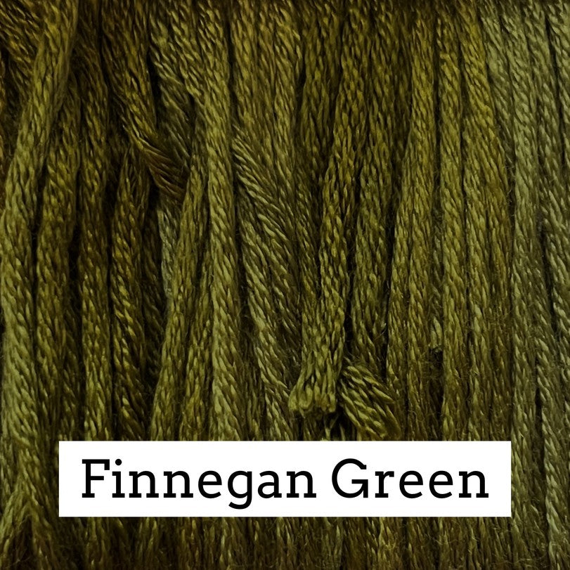 Close-up of olive‑green silk embroidery floss with subtle light and dark variegation, labeled “Finnegan Green.”