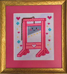 Framed cross stitch of a bright pink guillotine with a smiling cartoon face on the blade, surrounded by stitched hearts, stars, and diamonds on a light background, set within a gold frame and pink mat.