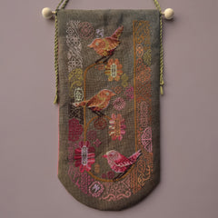 Cross stitched wall hanging featuring stylized birds perched among pink and orange flowers on a dark fabric background.