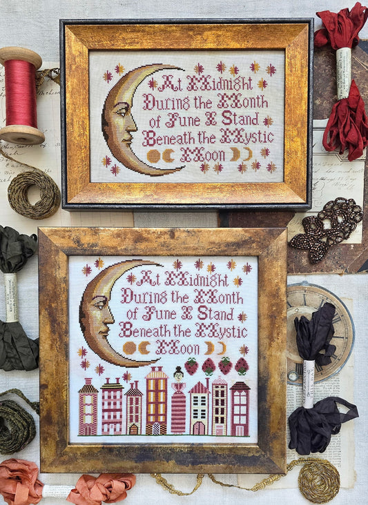 Framed cross-stitch samplers featuring a crescent moon face with decorative stars and stitched verse, with one design above a row of stylized houses, displayed with vintage sewing notions and ribbon.
