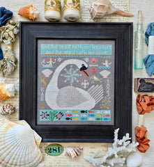 Framed cross-stitch sampler of a large white whale surrounded by small ocean motifs, including fish, shells, an anchor, a compass, and a bird, against a gray background with decorative borders.
