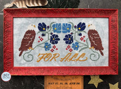 Cross stitch of two bald eagles flanking a floral motif in blue and red, with the words “For All” stitched in mustard yellow, framed in a red carved frame.
