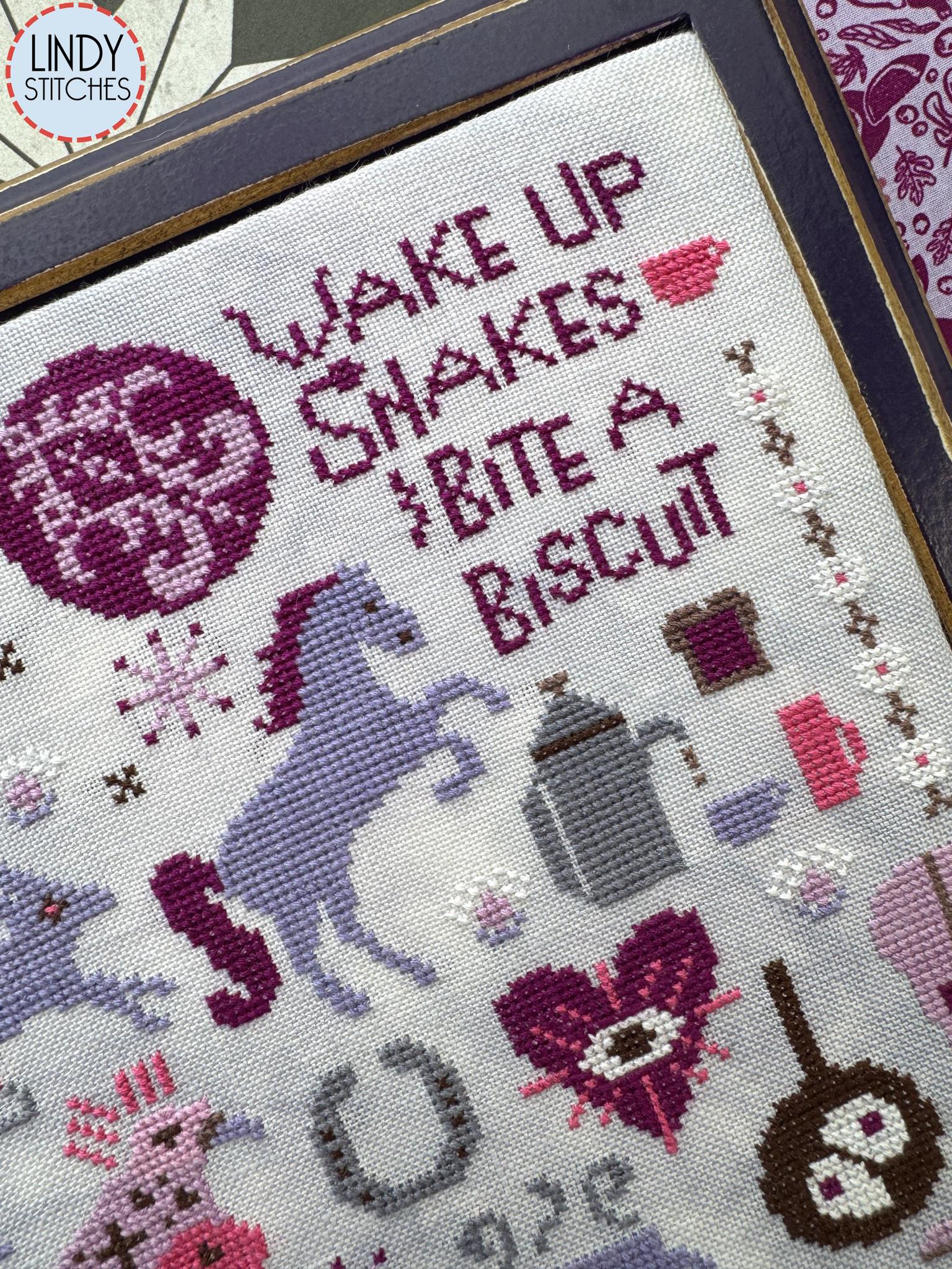 Close up view of same cross stitch with a zoom in on the text, “Wake up snakes, bite a biscuit.”