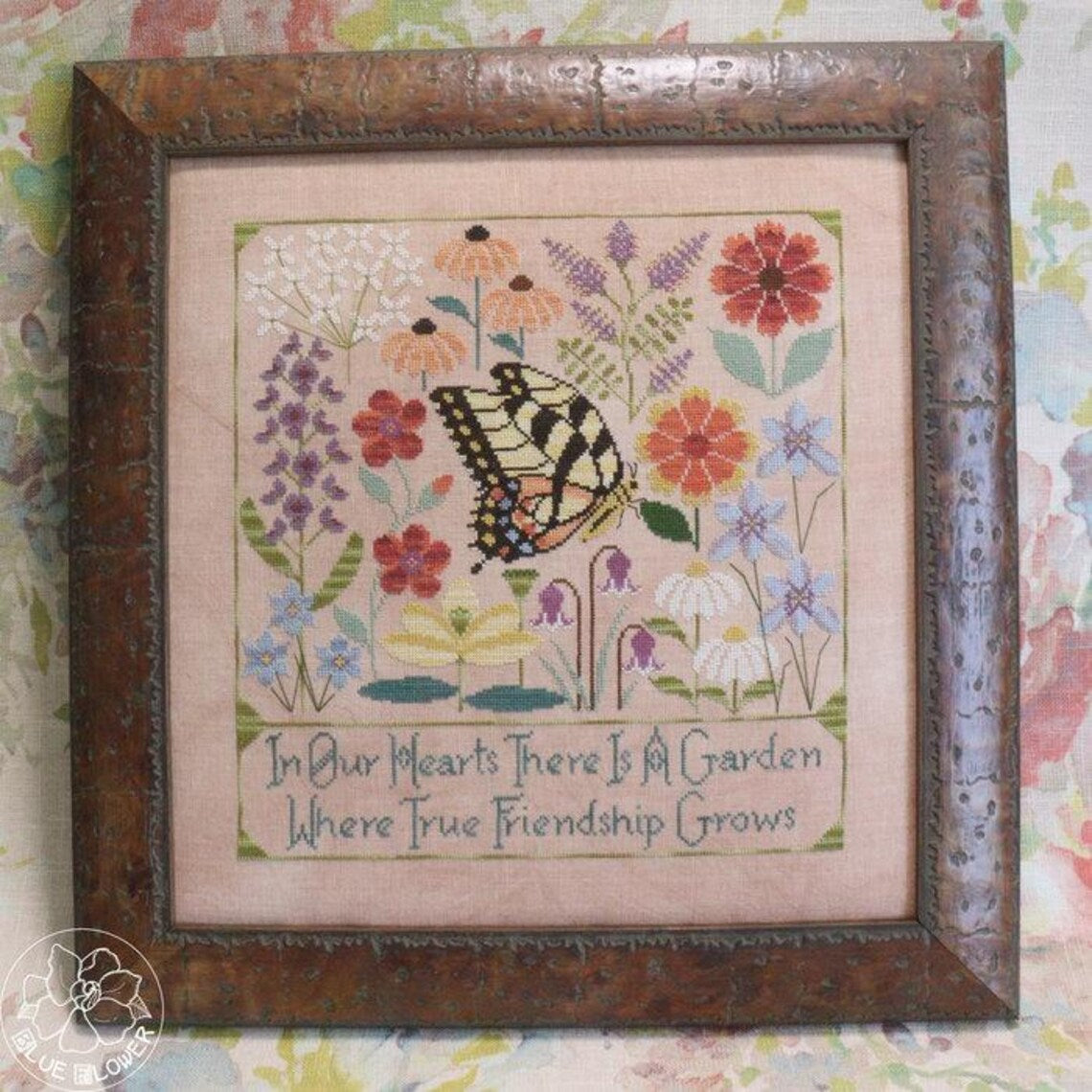 Framed cross stitch of a butterfly among colorful garden flowers with the text “In Our Hearts There Is A Garden Where True Friendship Grows.”