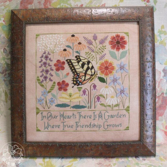 Framed cross stitch of a butterfly among colorful garden flowers with the text “In Our Hearts There Is A Garden Where True Friendship Grows.”