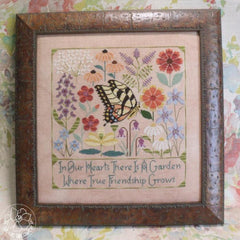 Framed cross stitch of a butterfly among colorful garden flowers with the text “In Our Hearts There Is A Garden Where True Friendship Grows.”
