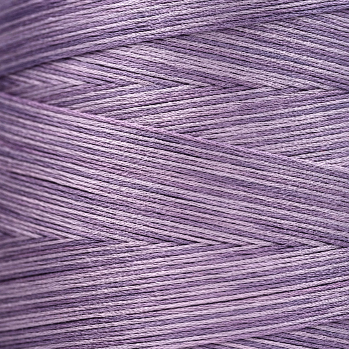 Close-up of lavender‑purple overdyed embroidery floss wound tightly, showing subtle shade variations in the strands.